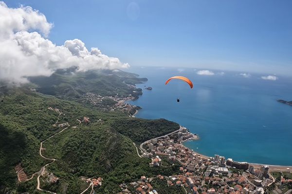 Paragliding Montenegro Budva – Flying with an orange canopy over Becici beach and the Adriatic coast.