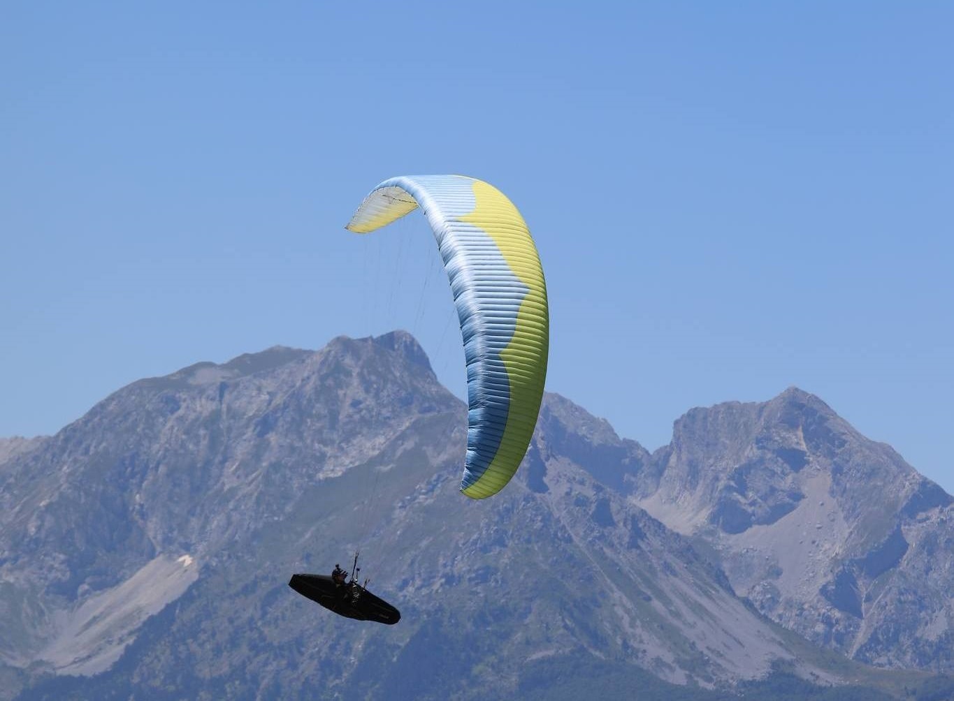 XC paragliding pilot flying a competition wing over the Komovi mountain range in Montenegro.